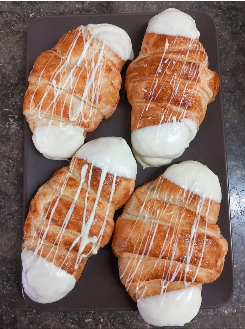 Quatre croissants de xocolata blanca amb un fil de xocolata per sobre, sobre una safata gris