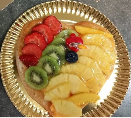 Pastís de fruita fresca amb maduixes, kiwi, pinya, nabius i mango, sobre un plat daurat